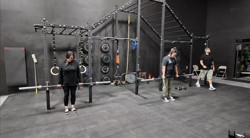Members holding barbells at the rig during a Strength & Conditioning group class